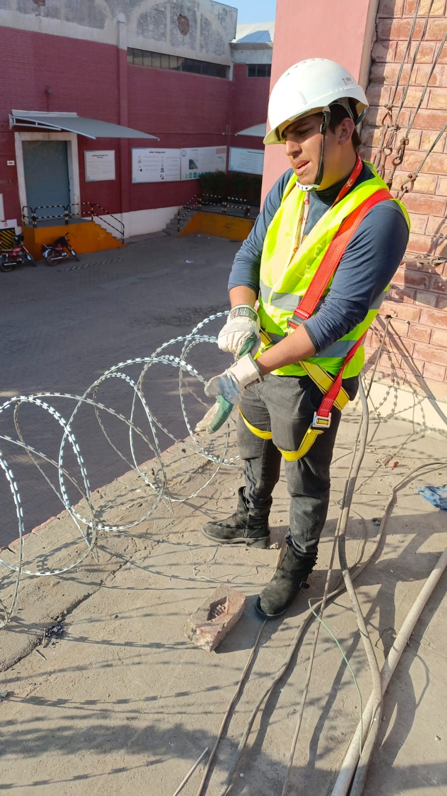 Worker handling concertina razor wire with full PPE and harness